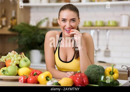 Donna sportiva mordente pomodoro ciliegia in casa cucina Foto Stock