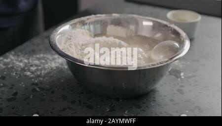 inumidire gli ingredienti nella farina in una ciotola d'acciaio sul piano di appoggio in calcestruzzo, foto ampia Foto Stock