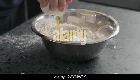 l'uomo aggiunge ingredienti bagnati nella farina in una ciotola d'acciaio sul ripiano in cemento, foto ampia Foto Stock