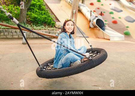 giovane donna che si diverte su un'oscillazione di mare al parco giochi urbano Foto Stock