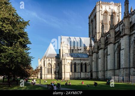 I visitatori seduti sull'erba fuori dal Minster di York in una giornata di sole in estate. York, Inghilterra, Regno Unito Foto Stock