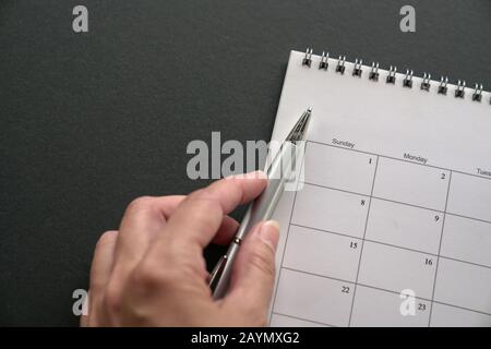 Calendario bianco su sfondo scuro con spazio di copia, Tenendo Una penna. Pianificazione di riunioni aziendali, fase cardine del progetto o pianificazione di viaggi o promemoria con Foto Stock