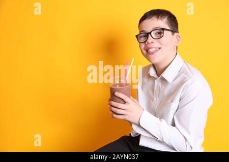 Un giovane ragazzo di 8yrs vecchio beve un bicchiere di latte al cioccolato su sfondo giallo Foto Stock