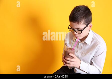 Un giovane ragazzo di 8yrs vecchio beve un bicchiere di latte al cioccolato su sfondo giallo Foto Stock