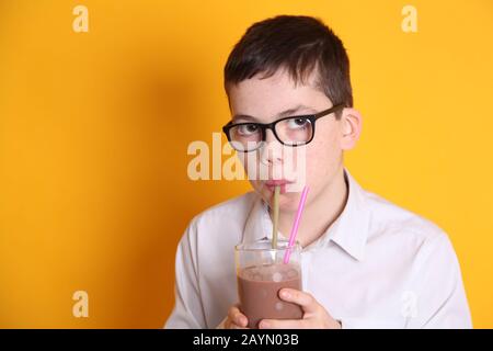 Un giovane ragazzo di 8yrs vecchio beve un bicchiere di latte al cioccolato su sfondo giallo Foto Stock