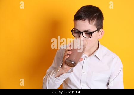 Un giovane ragazzo di 8yrs vecchio beve un bicchiere di latte al cioccolato con labbro superiore ricoperto di cioccolato su sfondo giallo Foto Stock