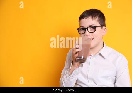 Un giovane ragazzo di 8yrs vecchio beve un bicchiere di latte al cioccolato su sfondo giallo Foto Stock