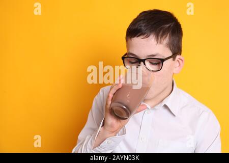 Un giovane ragazzo di 8yrs vecchio beve un bicchiere di latte al cioccolato su sfondo giallo Foto Stock