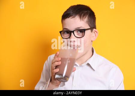 Un giovane ragazzo di 8yrs vecchio beve un bicchiere di latte al cioccolato su sfondo giallo Foto Stock