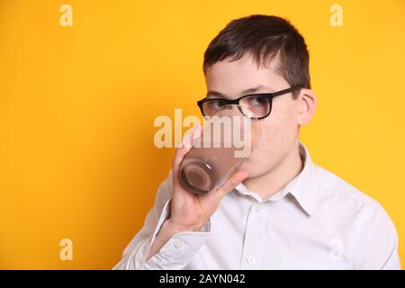 Un giovane ragazzo di 8yrs vecchio beve un bicchiere di latte al cioccolato su sfondo giallo Foto Stock