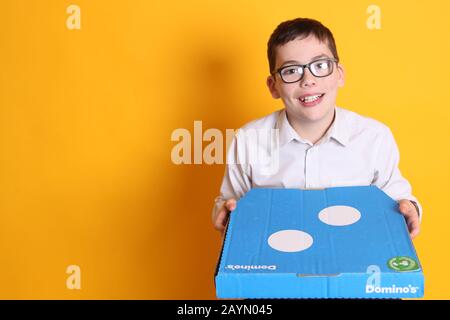 Un ragazzo giovane che indossa bicchieri di 12 anni con una scatola per la pizza di Domino su sfondo giallo Foto Stock