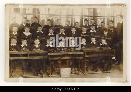 Cartolina edoardiana sbiadita di scolari in classe, seduta a file di scrivanie, modellazione argilla, al contrario è J.L. Maltby, Winchester, Hampshire, Inghilterra, U.K. circa 1905 Foto Stock