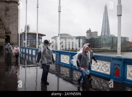 La gente attraversa il Tower Bridge, a Londra, durante un pesante rovescio di pioggia mentre Storm Dennis colpisce il Regno Unito. Foto Stock