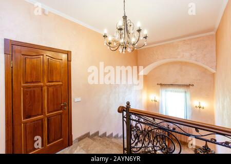 Scale nel cottage. Gradini in marmo, ringhiere in ferro battuto, corrimano in legno. Lampadario in ferro battuto. Porta di legno sul pianerottolo. Foto Stock