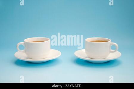 Due tazze di caffè bianco con latte, sfondo azzurro, vista laterale. Americano. Spazio di copia Foto Stock