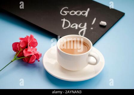 Concepimento Buongiorno. Lavagna in gesso nero con l'iscrizione buon giorno, una tazza di caffè rosa su uno sfondo blu chiaro. Disposizione piatta Foto Stock