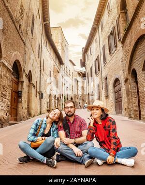 Gruppo eterogeneo di amici felici e positivi seduti nel centro storico della Toscana Foto Stock