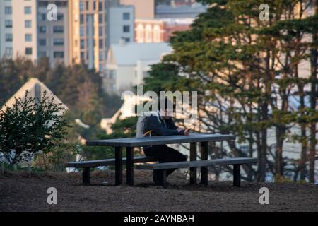 Un uomo siede da solo ad un tavolo in Alamo Square a San Francisco. Foto Stock