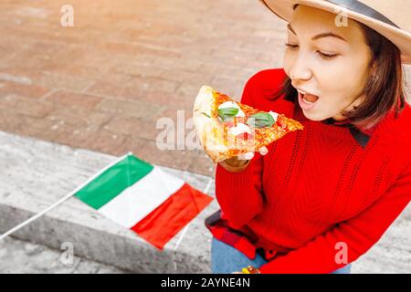 Donna felice che mangia pizza fetta in Italia, all'aperto. Viaggi in Europa e concetto di cibo italiano Foto Stock