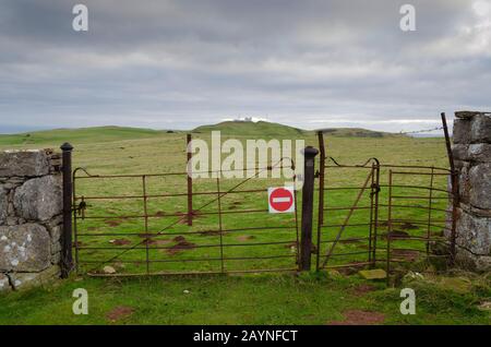 Un cancello arrugginito della fattoria ha un simbolo di entrata assente attaccato ad esso. Accanto al cancello si trova un arrugginito kissing gate. Entrambi i cancelli sono ricoperti da filo spinato. La posizione Foto Stock