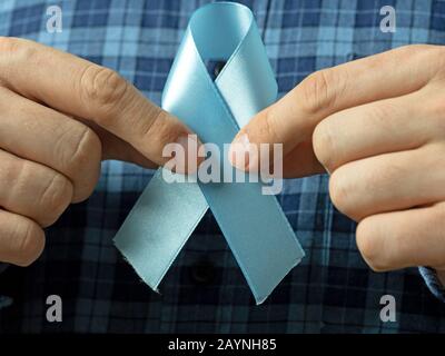 Un uomo in una camicia plaid tiene due mani blu Ribbon simbolo del cancro prostatico Awareness.Concept della medicina e mans assistenza sanitaria Foto Stock