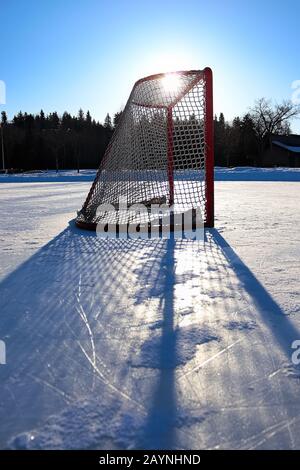 Sole che silhouette una rete vuota di hockey su uno stagno congelato Foto Stock