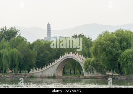 Vista sul Lago di Kunming verso un ponte di pietra e la collina della Primavera della Giada con la Pagoda del picco della Giada al Palazzo Estivo, che era il giardino imperiale di Qing D. Foto Stock
