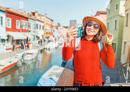 Giovane e felice viaggiatore donna che prende selfie tra case colorate sull'isola di Burano, Venezia. Concetto Turismo in Italia Foto Stock