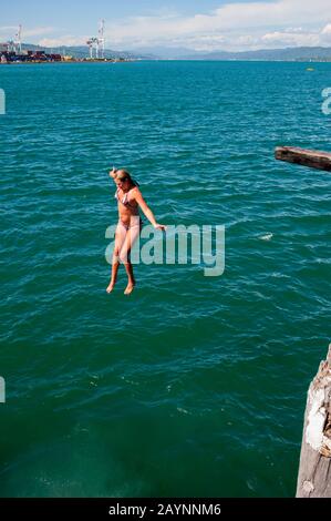 Una ragazza adolescente sta saltando in acqua lungo il lungomare nella baia del porto di Lambton, parte del porto di Wellington, che è il grande naturale Foto Stock