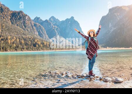 Felice giovane viaggiatore donna divertirsi su una costa di un lago Dobbiaco nelle Alpi Dolomiti, Italia Foto Stock