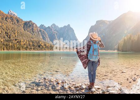 Felice giovane viaggiatore donna divertirsi su una costa di un lago Dobbiaco nelle Alpi Dolomiti, Italia Foto Stock