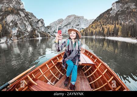 Felice donna asiatica prendere selfie con smartphone in una barca in un lago di montagna durante la stagione autunnale Foto Stock