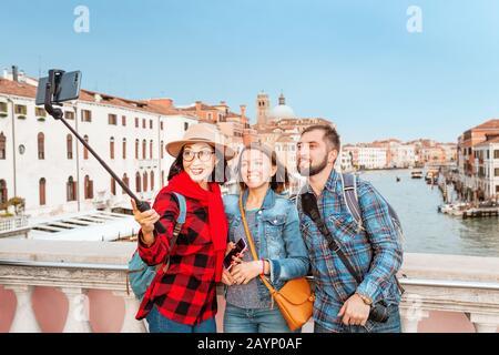 Felice gruppo di amici viaggiatori che fanno selfie con selfie bastone sullo sfondo del Canal Grande a Venezia, Italia Foto Stock