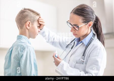 La donna del medico misura la temperatura del ragazzo giovane in ufficio medico. Foto Stock