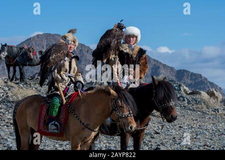 Due ragazze adolescenti di cacciatori di aquila kazaka e le loro aquile d'oro a cavallo sulla strada per il Festival dell'aquila d'oro vicino alla città di Ulgii (Ölgii) Foto Stock