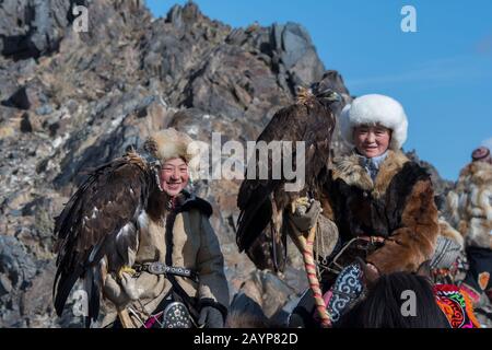 Due ragazze adolescenti di cacciatori di aquila kazaka e le loro aquile d'oro a cavallo sulla strada per il Festival dell'aquila d'oro vicino alla città di Ulgii (Ölgii) Foto Stock