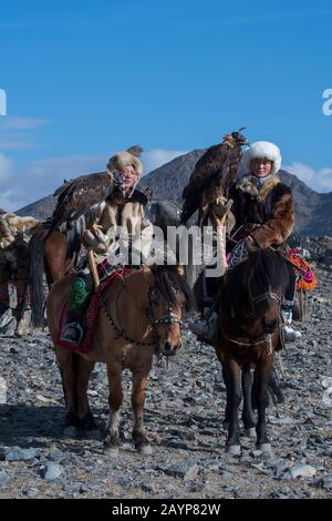 Due ragazze adolescenti di cacciatori di aquila kazaka e le loro aquile d'oro a cavallo sulla strada per il Festival dell'aquila d'oro vicino alla città di Ulgii (Ölgii) Foto Stock