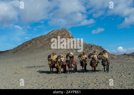 Un gruppo di cacciatori di aquila kazaka e le loro aquile d'oro a cavallo sulla strada per il Festival dell'aquila d'oro vicino alla città di Ulgii (Ölgii) nella baia Foto Stock