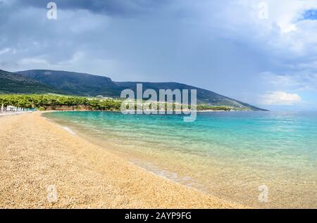 Spiaggia di ghiaia Zlatni Rat o Corno d'Oro o Capo d'Oro a Bol città, Brac Island, Croazia. Spiaggia di ghiaia, montagna e acque turchesi del Mare Adriatico Foto Stock