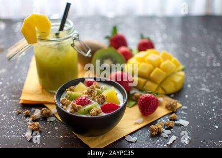 colazione sana: yogurt con crocchette, fragole fresche, kiwi, mangoes e fiocchi di cocco con. Servito con un frullato verde in un vaso Foto Stock
