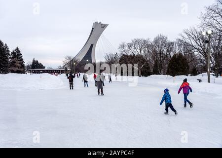 Montreal, CA - 15 febbraio 2020: Pattinaggio su ghiaccio al parco Maisonneuve pista di pattinaggio su ghiaccio con olympic Stadium Tower sullo sfondo. Foto Stock