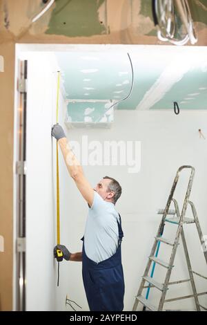 Vista laterale ritratto di operaio edile senior misurazione muro mentre ristrutturazione casa Foto Stock