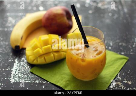 Delizioso frullato con mango in un bicchiere di ghiaccio tritato e frutta Fresca in paglia sullo sfondo Foto Stock
