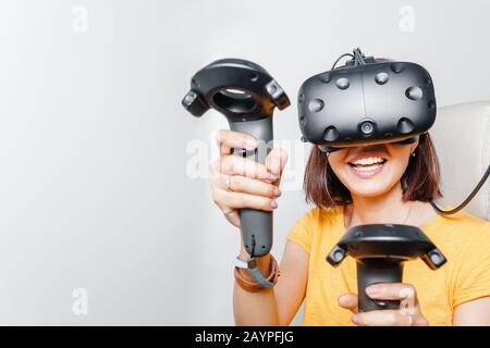 Donna felice con visore per la realtà virtuale e joystick che gioca ai videogame VR Foto Stock