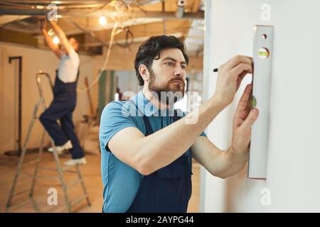 Ritratto di operaio edile con bearded che misura il livello di parete mentre ristruttura casa, copia spazio Foto Stock