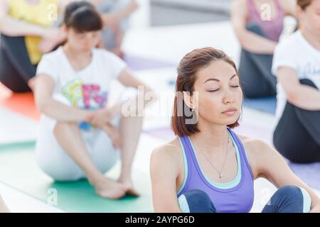 Gruppo di felici cute giovani donne seduta e stretching in asana yoga posa, meditazione e allenamento concetto di allenamento Foto Stock