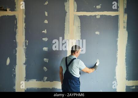 Vista posteriore ritratto di uomo anziano che lavora su parete asciutta mentre ristrutturando casa, copia spazio Foto Stock