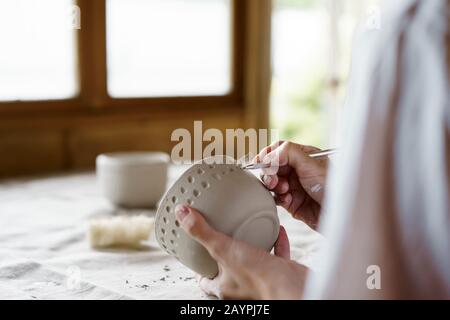 Mani femminili tenere una ciotola per il colaggio di prodotti di argilla Foto Stock