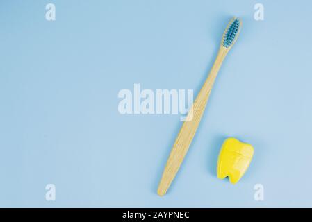 Spazzola di legno di bambù e filo interdentale in forma di dente su sfondo blu. Concetto di cura orale. Copyspace. Foto Stock