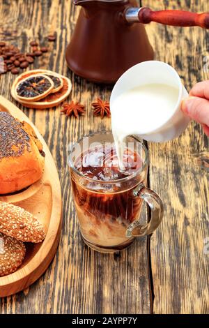 Nel caffè espresso appena fatto in una tazza di vetro trasparente, la crema viene versata da una tazza bianca sullo sfondo di un vecchio tavolo di legno Foto Stock